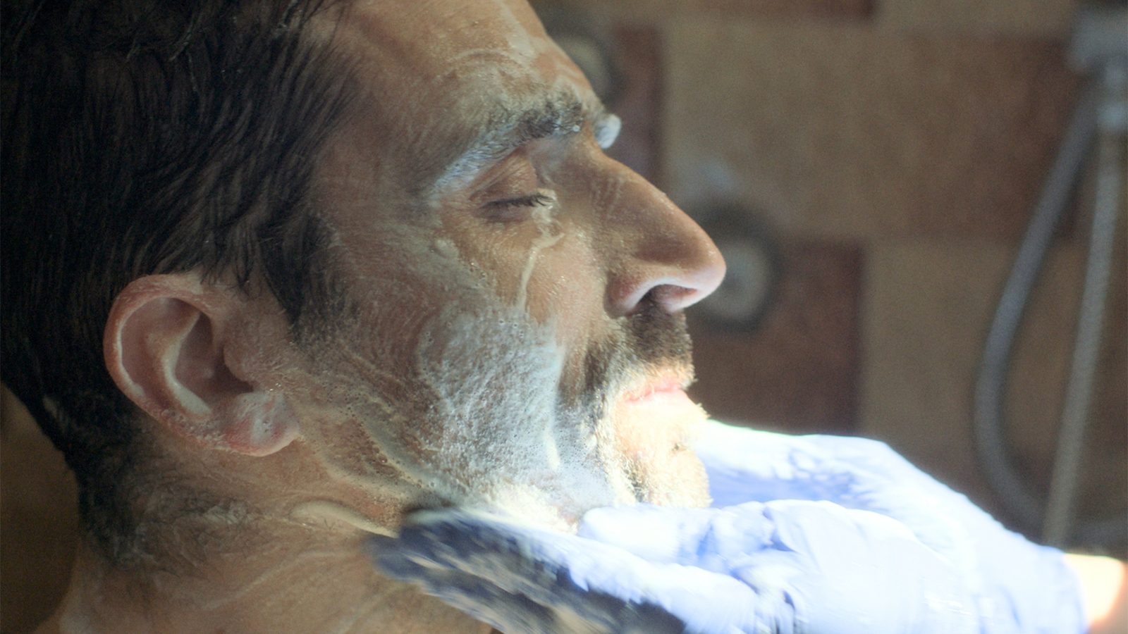 A close-up profile of Mickey mid-shave, in a still from Another Body
